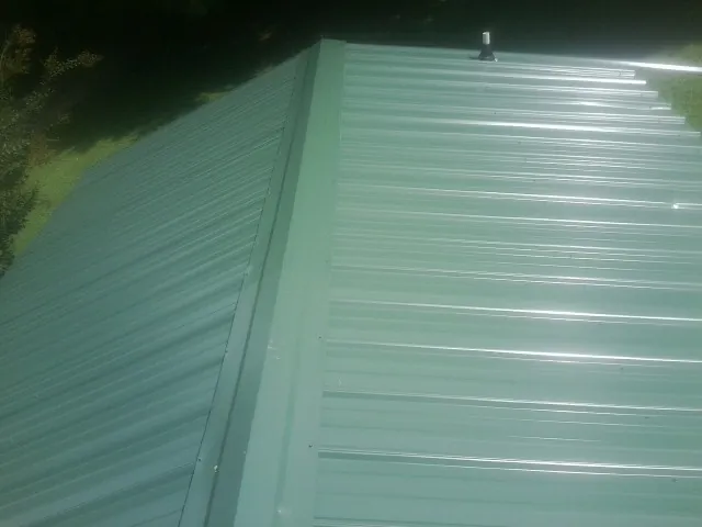 New green metal panels meeting at the ridge of a roof — Flat Roof Repair work by our crew in Salvisa