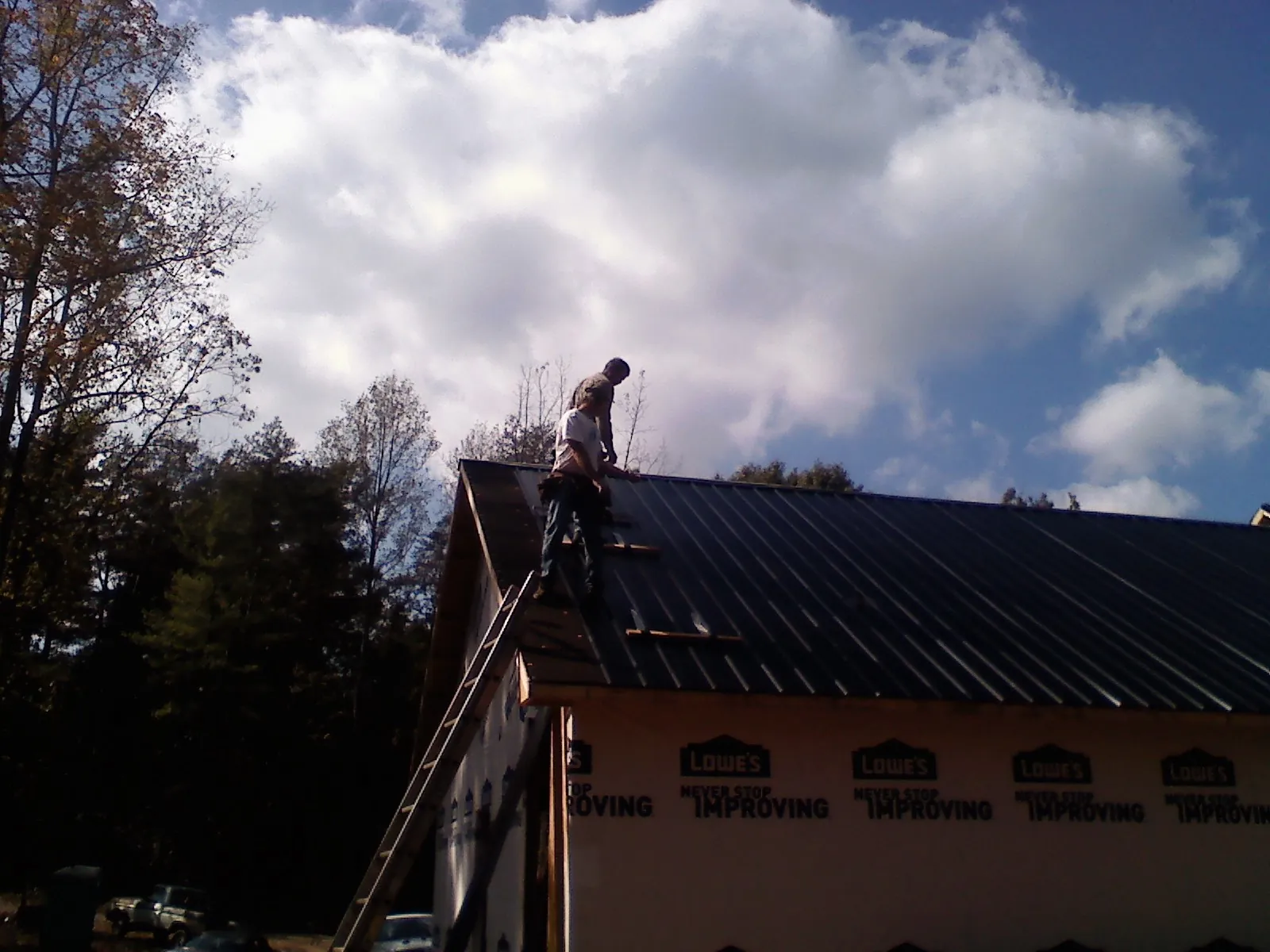 Roofer fastening dark metal panels high against a cloudy sky, from a Roof Inspection job in Salvisa